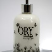 ORY Botanical Garden glass lotion bottle with soft ivory glass, delicate wildflower illustrations, and polished silver pump for personalized skincare.