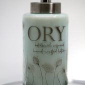 ORY Serenity Blue botanical glass lotion bottle with soft blue tint, delicate floral line illustrations, and brushed silver pump for personalized skincare.