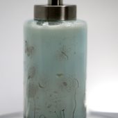 ORY Serenity Blue botanical glass lotion bottle with soft blue tint, minimalist floral line art, and brushed silver pump for personalized skincare.