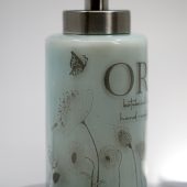 ORY Serenity Blue botanical glass lotion bottle with soft blue tint, delicate floral line illustrations, and brushed silver pump for personalized skincare.