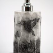 ORY Midnight Garden marble lotion bottle with etched hummingbird and floral illustrations, sculpted stone-finish glass and polished silver pump for personalized skincare.