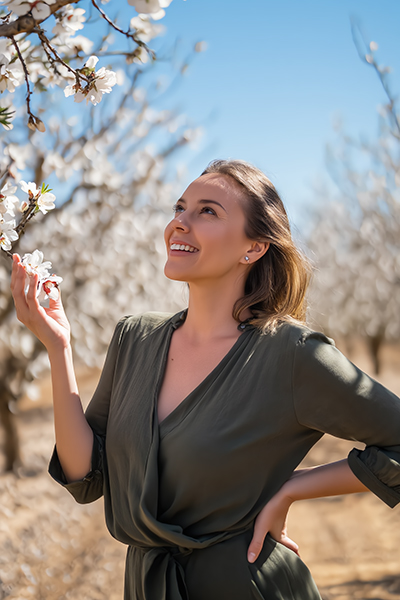 Woman in a blooming almond orchard with radiant, nourished skin, symbolizing the gentle moisturizing and soothing benefits of sweet almond oil in skincare.