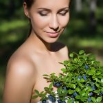 Woman holding fresh wild bilberries and green leaves outdoors, representing wild bilberry extract used in ORY Skincare for antioxidant and skin-brightening benefits.