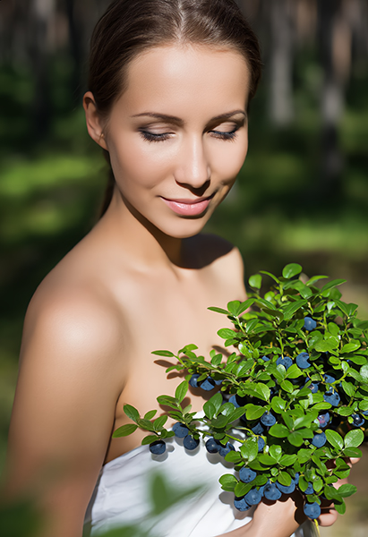 Woman holding fresh wild bilberries and green leaves outdoors, representing wild bilberry extract used in ORY Skincare for antioxidant and skin-brightening benefits.