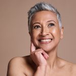 Smiling mature woman with radiant, healthy skin touching her face — ORY Skincare mature skincare for hydration, firmness, and radiance.