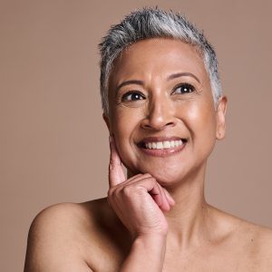 Smiling mature woman with radiant, healthy skin touching her face — ORY Skincare mature skincare for hydration, firmness, and radiance.