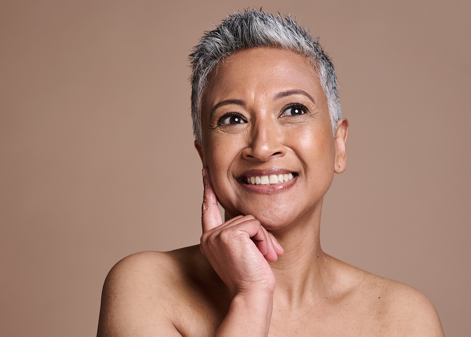 Smiling mature woman with radiant, healthy skin touching her face — ORY Skincare mature skincare for hydration, firmness, and radiance.