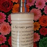 Handcrafted ORY Skincare lotion bottle with engraved message, surrounded by vibrant botanical flowers, symbolizing love, intention, and artisanal skincare.