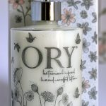 Elegant personalized ORY botanical infused hand and body lotion bottle with pump dispenser, featuring leaf and butterfly designs on floral background, showcasing Oryskincare's custom natural skincare solutions for nourished, hydrated skin.
