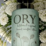 Elegant personalized ORY botanical infused hand and body lotion bottle with pump dispenser, featuring leaf and butterfly designs on floral background, showcasing Oryskincare's custom natural skincare solutions for nourished, hydrated skin.