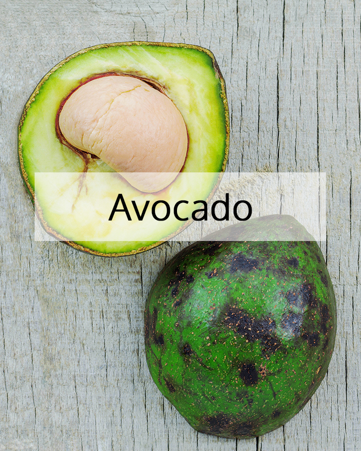 Fresh avocado cut in half showing the seed and vibrant green flesh on a rustic wooden surface, representing the nourishing source of avocado oil used in ORY Skincare.
