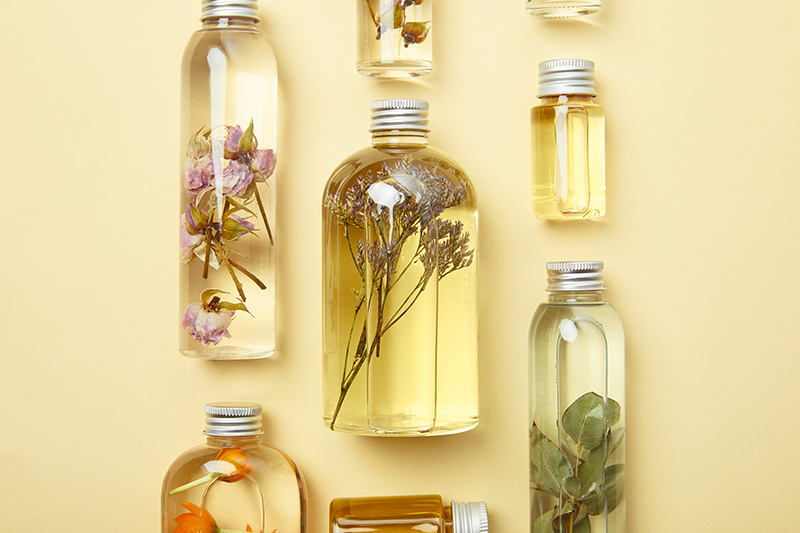 Assorted glass bottles filled with botanical-infused oils and preserved flowers, showcasing ORY Skincare’s handcrafted botanical infusion process.