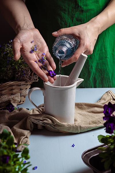 Handcrafted botanical infusion with fresh violet flowers and liquid extract poured into a ceramic mortar, showcasing ORY Skincare’s artisanal infusion process.