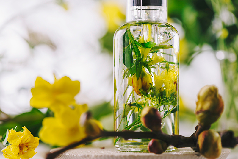 Glass bottle containing fresh yellow botanicals and green stems infused in oil, illustrating ORY Skincare’s handcrafted botanical infusion process.