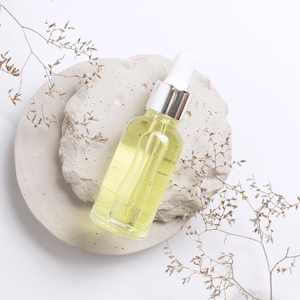 Glass dropper bottle containing pale yellow botanical-infused oil resting on natural stone, representing ORY Skincare’s low-heat botanical infusion method designed to preserve plant potency and skin benefits.