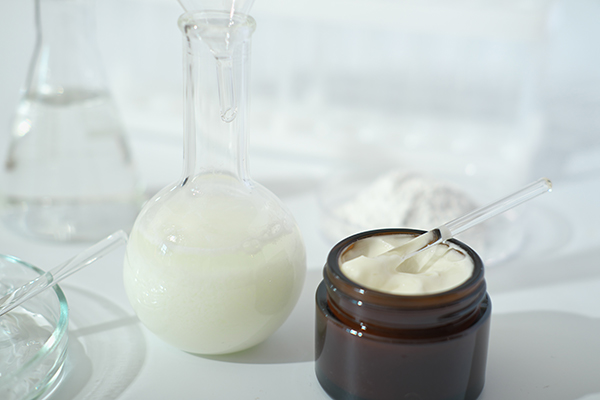 Laboratory glassware and cream formulation illustrating emulsifier science in skincare, blending oil and water phases for stable cosmetic emulsions.