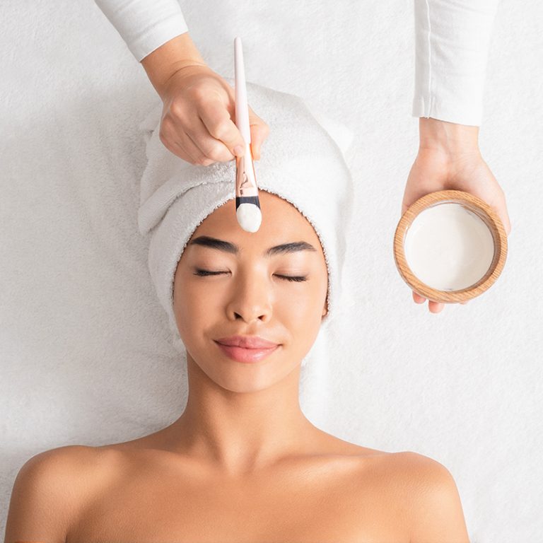 Facial treatment demonstrating emulsifier science as a cream mask is applied with a brush, showing smooth blending of oil and water phases for balanced, hydrated skin.