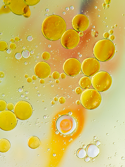 Golden oil droplets suspended in water illustrating emulsifier science and oil-water interaction in advanced skincare formulation.