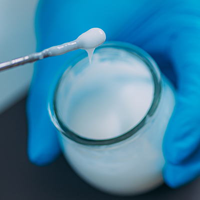 Laboratory emulsifier science in skincare formulation, showing a gloved hand blending a creamy oil-water emulsion for stable botanical skincare products.