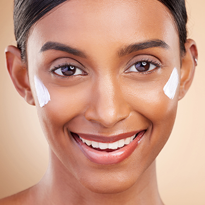 Woman with radiant skin applying a lightweight emulsified skincare cream to the cheeks, demonstrating advanced emulsifier science in ORY Skincare formulations.