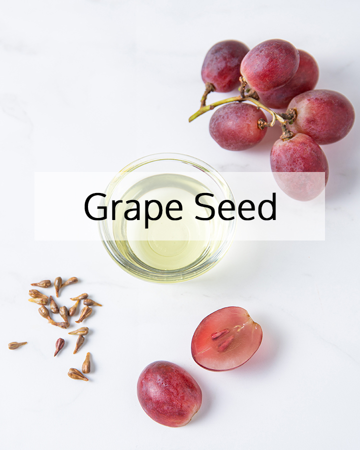 Grape seed oil in a glass bowl with fresh red grapes and grape seeds on a white background, representing the antioxidant-rich source used in ORY Skincare for lightweight hydration and skin protection.