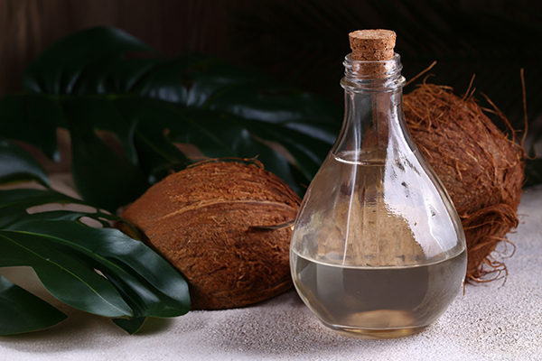 Glass bottle of coconut and palm oil beside whole coconuts and tropical leaves — natural moisturizing oils for ORY Skincare.
