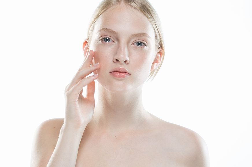 Woman with clear, balanced skin gently touching her face against a white background, representing healthy skin and skincare for all skin types.