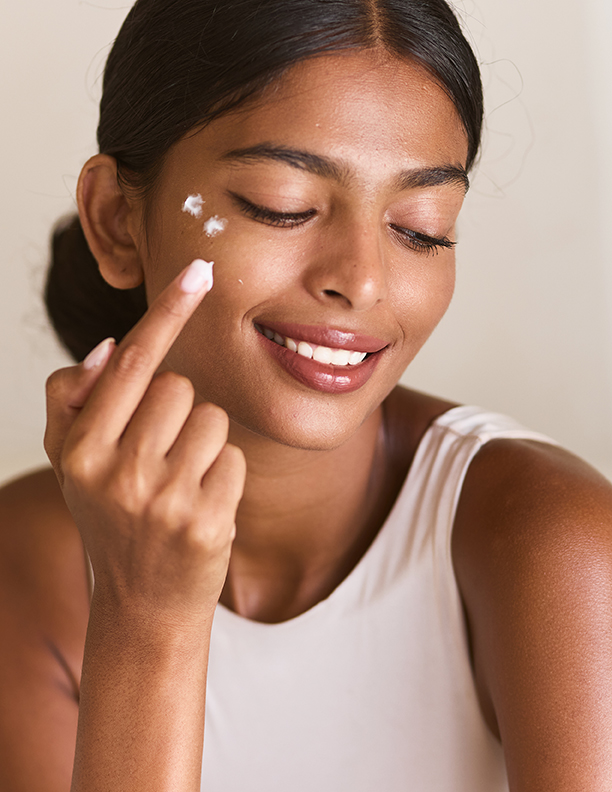 Woman gently applying facial cream to her cheek during a skincare routine, highlighting hydrated, radiant skin and mindful self-care with ORY Skincare.