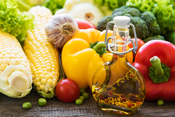 Cold-pressed botanical oil surrounded by fresh vegetables and herbs, representing naturally derived emulsifier science in ORY Skincare formulations.