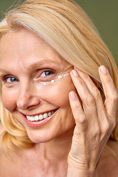 Smiling mature woman applying eye cream, showcasing hydrated and youthful skin for ORY Skincare’s mature skincare collection.