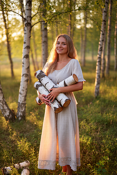Woman holding birch logs in a sunlit forest — natural birch bark extract skincare ingredient for ORY Skincare.