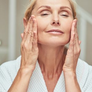 Mature woman cleansing and massaging her face, representing ORY Skincare’s hydrating and firming cleanser for mature skin.