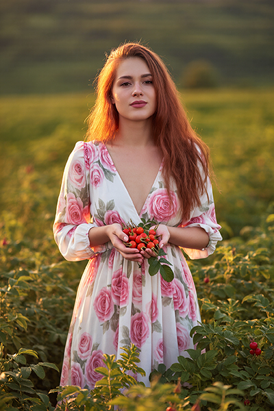 Woman holding fresh rosehips in a field, representing rosehip extract as a natural ORY Skincare ingredient rich in antioxidants and skin-nourishing nutrients.