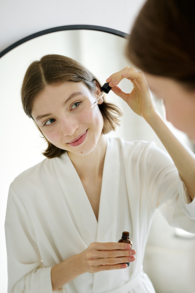 Woman applying bi-phasic facial oil serum in front of a mirror, demonstrating ORY Skincare’s bi-phasic infusion method that blends botanical oils and water-based actives for balanced hydration and nourishment.