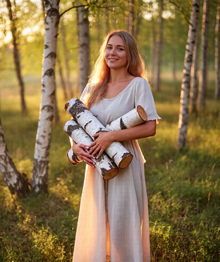 Woman holding birch logs in a sunlit forest — natural birch bark extract skincare ingredient for ORY Skincare.