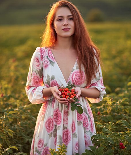 Woman holding fresh rosehips in a field, representing rosehip extract as a natural ORY Skincare ingredient rich in antioxidants and skin-nourishing nutrients.