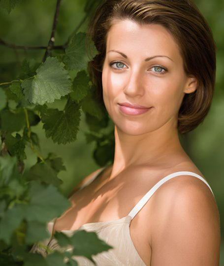 Woman with clear, balanced skin standing among green leaves, representing Witch Hazel Extract used in ORY Skincare for soothing, toning, and refining pores.