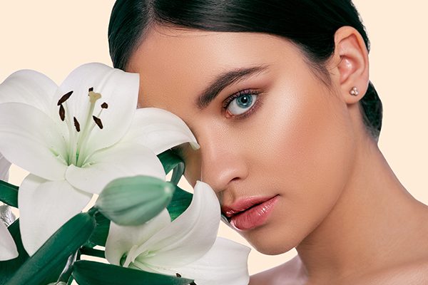 Woman with radiant, healthy skin holding white lily flower, representing a gentle botanical skincare routine by ORY Skincare.